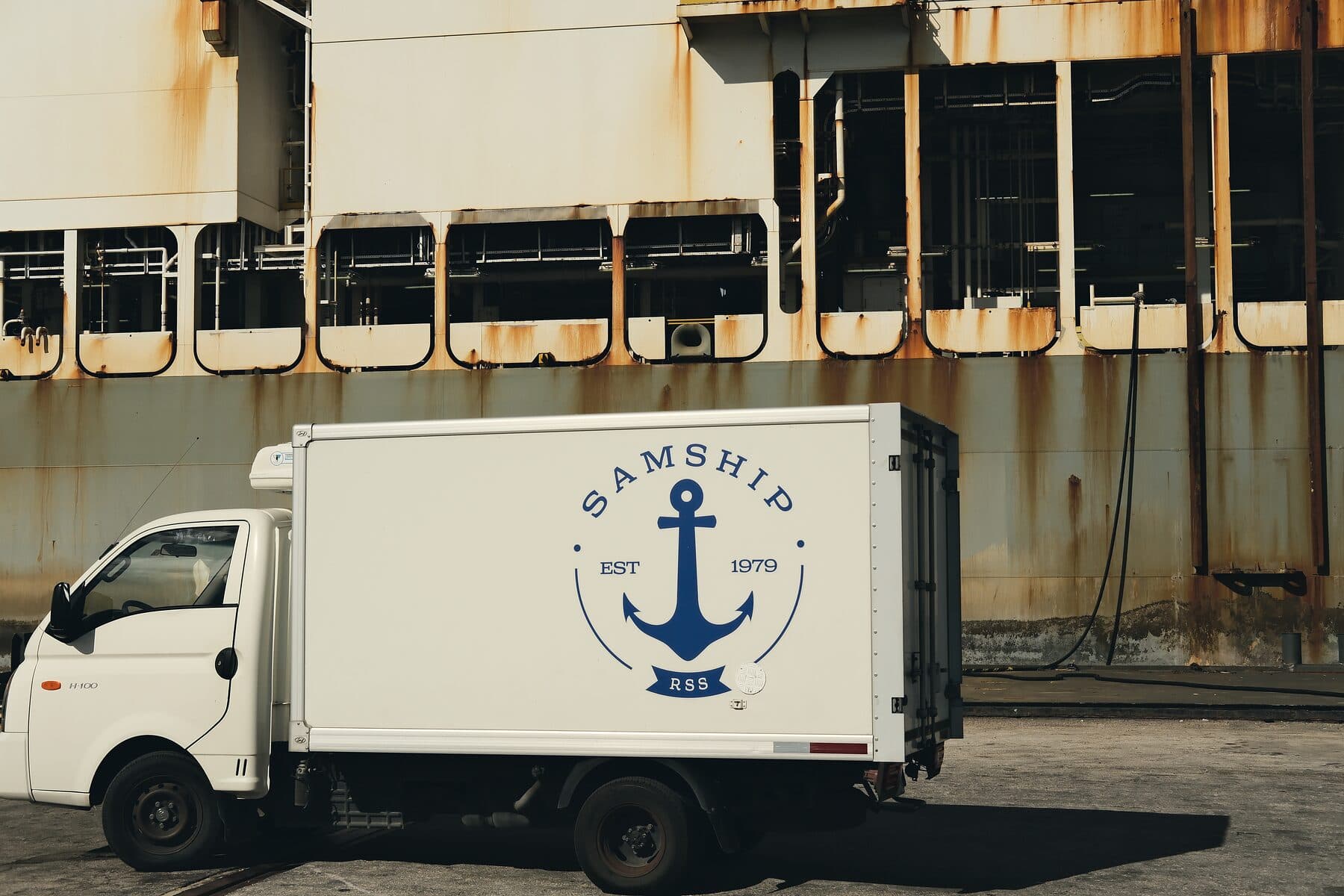 A Samship delivery truck with the crest on its side, parked on the quay alongside a vessel's hull